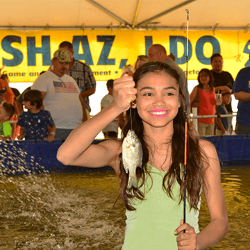 A girl smiles while holding up a fish she caught at the Arizona Game and Fish Outdoor Expo family fishing tank.